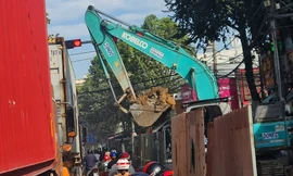 Gầu máy xúc đầy đất lơ lửng trên đầu người đi đường