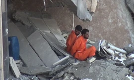 Hai tù nhân mặc áo cam bị trói ngồi bên trong ngôi nhà chờ chết