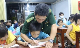 Thiếu tá Nguyễn Văn Tưởng ân cần kèm từng nét chữ cho các em tại lớp học tình thương. Ảnh: KHÁNH NGUYÊN
