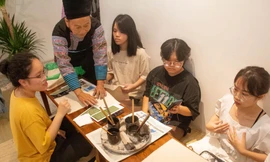 Nghệ nhân dân tộc Mông giàu kinh nghiệm dệt thổ cẩm hướng dẫn các bạn trẻ vẽ sáp ong. Ảnh: Bảo Thu