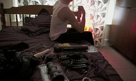 Oz ngồi trên giường bày công cụ làm việc. Ảnh: Metro.