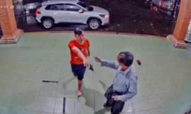 Người mặc áo đỏ cầm vật giống cây súng chĩa vào hai phụ nữ đối diện - ảnh chụp màn hình