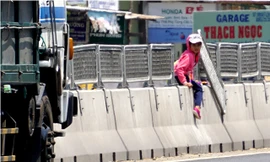 Một em học sinh tiểu học đang leo qua dải phân cách, ở vị trí lưới chống lóa bị tháo gỡ.