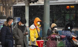 Người dân đeo khẩu trang chờ xe tại một ngã tư trong một buổi sáng tuyết rơi ở Bắc Kinh, ngày 19/1. Ảnh: AP 
