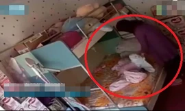 Bảo mẫu dùng khăn trùm kín đầu em bé 7 tháng tuổi. Ảnh cắt từ clip