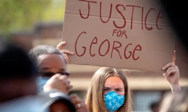 Người biểu tình cầm quốc kì Mỹ đi qua một tòa nhà bị đốt cháy ở Minneapolis. Ảnh: AP