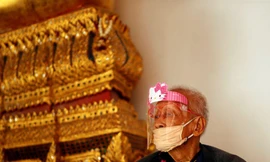 Một cụ ông đeo khẩu trang và tấm chắn ngồi trong một ngôi đền ở Bangkok. Ảnh: Reuters