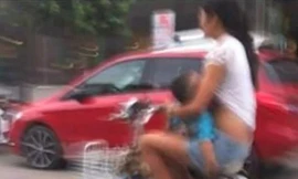 Người mẹ trẻ vừa đi xe đạp vừa cho con bú trên đường phố Trung Quốc