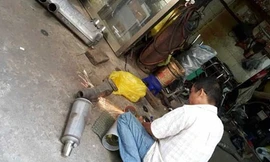 Một thợ đang cắt, độ lại pô mô tô tại tiệm ông H.