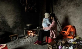 Chị Xie Xianmei ôm con trai khi đang ngồi đun bếp trong gia đình bố mẹ nuôi ở Dazhou. (Ảnh: Bloomberg)