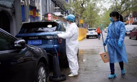 Một phụ nữ mặc đồ bảo hộ y tế trong khi rửa xe ô-tô trên đường phố ở Vũ Hán. (Ảnh: Reuters)