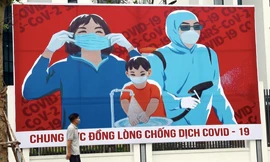 Một người đàn ông đi qua tấm áp phích kêu gọi người dân đoàn kết chống COVID-19. (Ảnh: Xinhua)