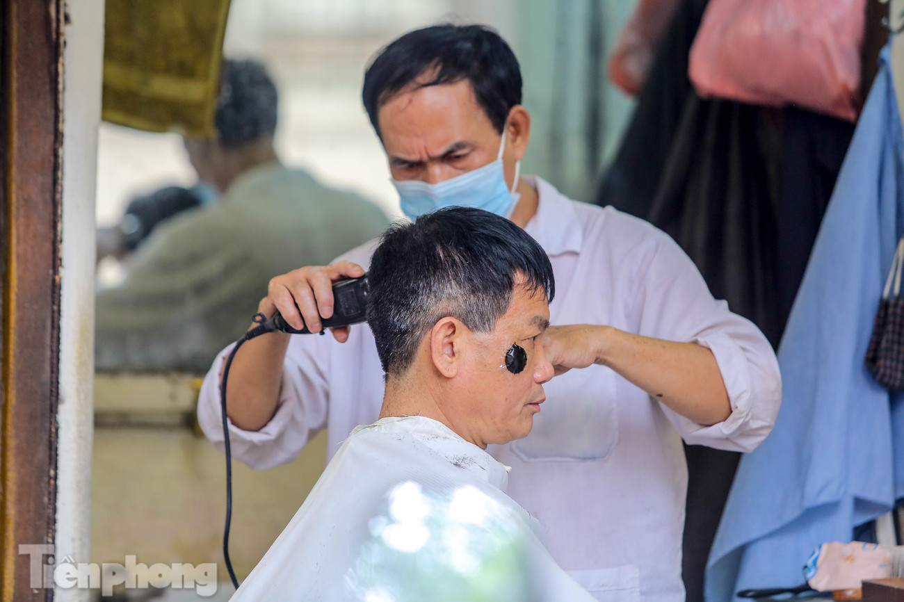 Một thợ cắt tóc ở phố Tràng Thi tranh thủ cắt cho khách quen trước giờ đóng cửa.