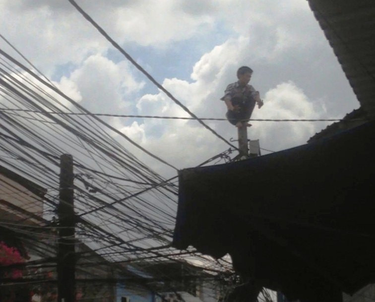 Nam thanh niên ngồi chồm hổm trên ngọn trụ điện.
