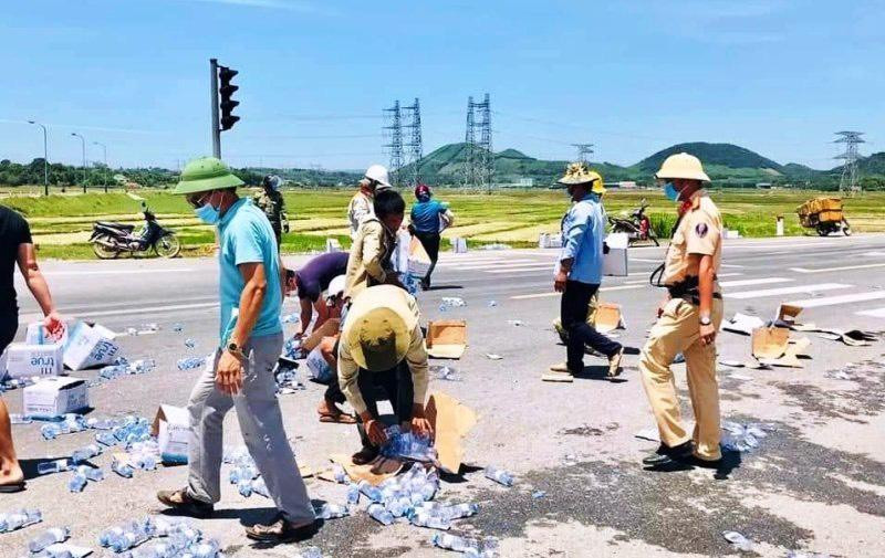 Xe container bị lật, chiến sĩ CSGT giúp thu gom hàng trăm thùng nước đổ giữa đường