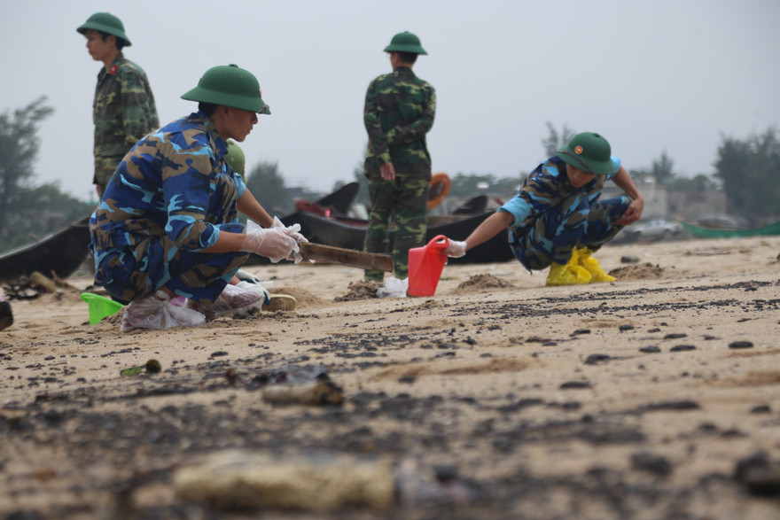Lực lượng chức năng được huy động đến thu gom lượng cặn dầu trên cát để đem đi xử lý
