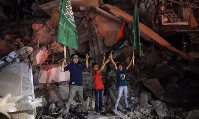 Trẻ em Palestine vẫy cờ Palestine và Hamas khi đang đứng trên đống đổ nát để bày tỏ vui mừng với thỏa thuận ngừng bắn ở Gaza ngày 21/5. Ảnh: AP