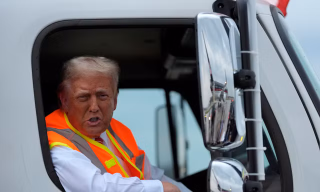 Ông Trump ngồi trên chiếc xe chở rác màu trắng in tên ông. (Ảnh: AP)