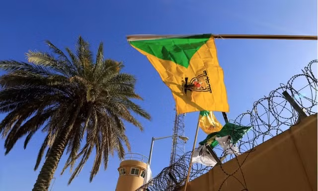 Một thành viên của lực lượng bán quân sự Hashd al-Shaabi giương cờ của nhóm dân quân Kataib Hezbollah trong cuộc biểu tình bên ngoài Đại sứ quán Mỹ ở Baghdad ngày 31/12/2019. (Ảnh: Reuters)