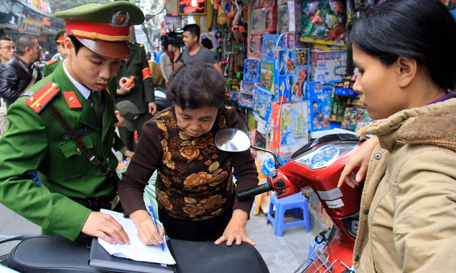 Một chủ hộ kinh doanh trên phố Lương Văn Can ký biên bản nộp phạt vì hành vi lấn chiếm vỉa hè. Ảnh: Trường Phong