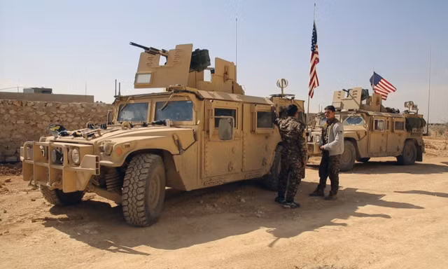 Chiến binh SDF đứng cạnh xe quân sự của Mỹ ở ngoại ô thị trấn Manbij, Aleppo, Syria, hồi tháng 3. Ảnh: AP