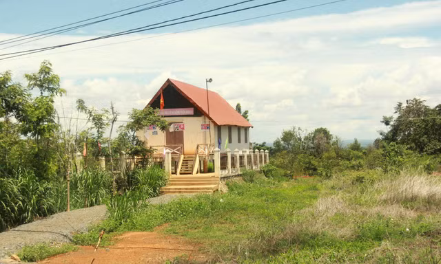 Nhà cộng đồng trơ trọi giữa bãi đất trống cỏ mọc um tùm 