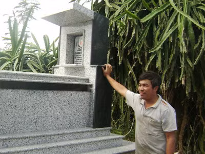 Anh Châu Văn Đông đứng bên mộ vợ, chị Đinh Thị Lan đã chết do bị điện giật ở vườn thanh long Ảnh: Châu Thành