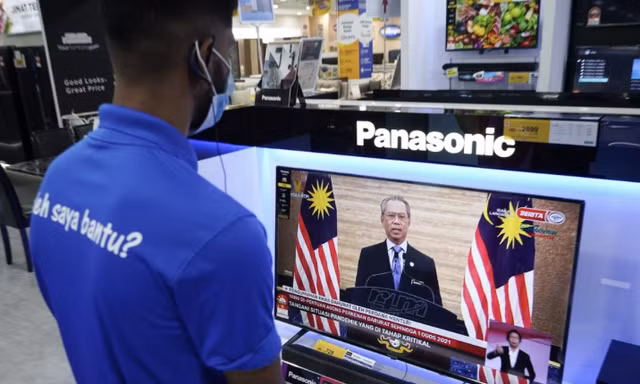 Nhân viên một cửa hàng điện tử ở Kuala Lumpur xem Thủ tướng Muhyiddin phát biểu trên truyền hình ngày 12/1. (Ảnh: AP)