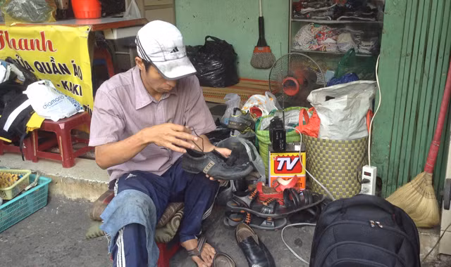 Anh Bình đang sửa giày cho một người bán vé số