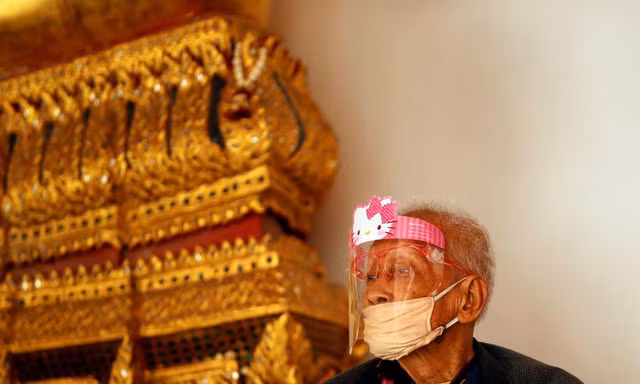 Một cụ ông đeo khẩu trang và tấm chắn ngồi trong một ngôi đền ở Bangkok. Ảnh: Reuters