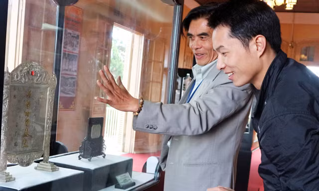 Giám đốc bảo tàng (bên trái) nói về bức trấn phong “vạn thọ tứ tuần Đại Khánh”.