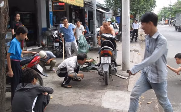 Nhiều người vây quanh xe máy để truy tìm con rắn.