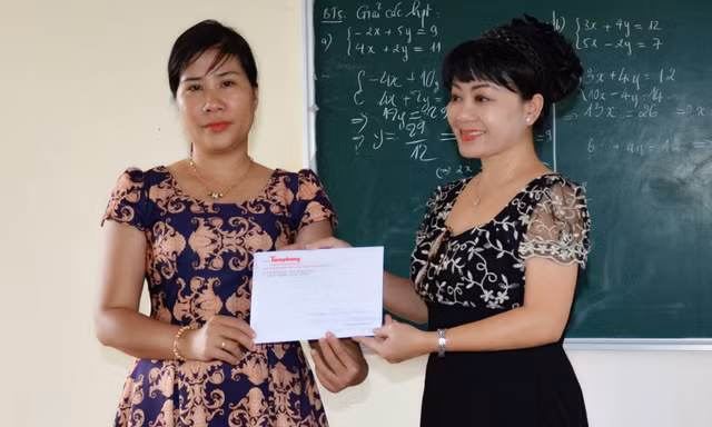 Cô Hồng Phượng (bên trái) nhận tiền hỗ trợ bữa ăn cho trò nghèo từ đại diện báo Tiền Phong