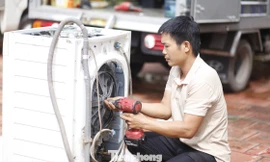 Một người thợ đang sửa máy giặt bị hỏng do nước lũ giúp người dân. Ảnh: Nguyễn Thắng