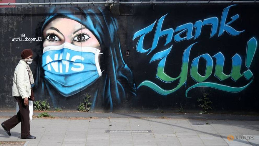 Một người dân London (Anh) đi ngang bức tranh tường vinh danh các nhân viên y tế. Ảnh: Reuters