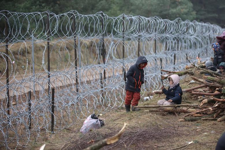 Trẻ em ngồi chơi cạnh hàng rào ngăn cách giữa Belarus và Ba Lan. Ảnh: Reuters