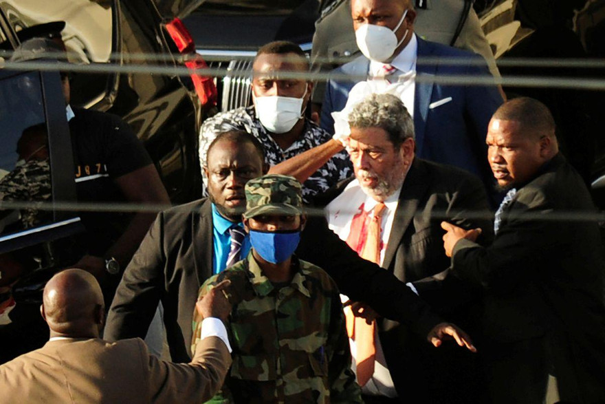 Ông Ralph Gonsalves (mắc sơ mi trắng) được các vệ sĩ đưa đi sau khi bị tấn công vào đầu. Ảnh: Reuters