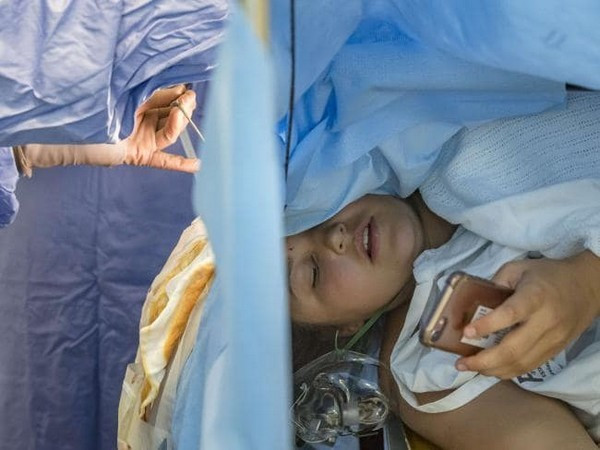 Jess Banik đang sử dụng điện thoại trong khi các bác sĩ đang tiến hành ca phẫu thuật não cho cô