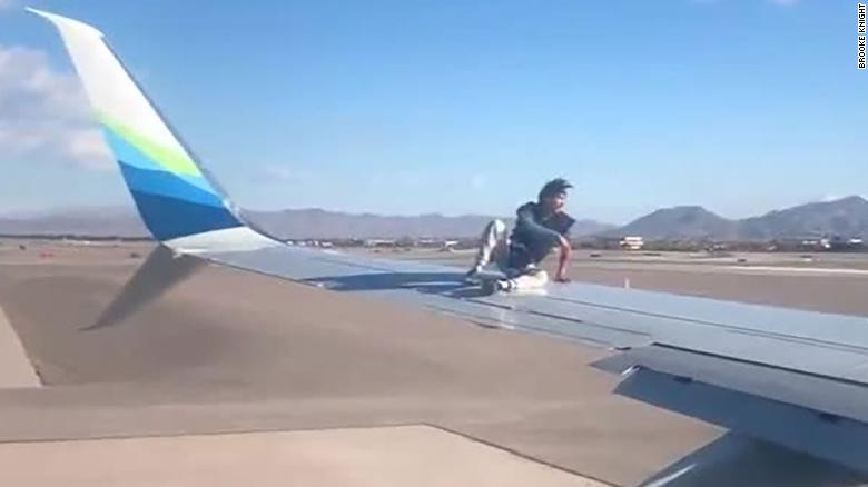 Người đàn ông chưa rõ danh tính ngồi vắt vẻo trên cánh chiếc máy bay chuẩn bị cất cánh. 