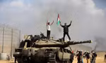 Người Palestine vẫy quốc kỳ của họ và ăn mừng bên một chiếc xe tăng Israel bị tịch thu trên Dải Gaza ngày 7/10. (Ảnh: AP)