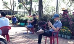 Vắng khách, người bán hoa Tết ngồi nghịch điện thoại giết thời gian.