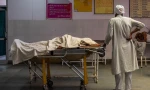 Một người đàn ông Ấn Độ đứng cạnh thi thể vợ qua đời vì COVID-19. Ảnh: Reuters