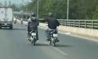 2 người đi xe máy khoác vai nhau chạy trên làn ôtô