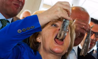 Thủ tướng Đức Angela Merkel há miệng ăn cá trích ngâm sau lễ đặt tên cho chiếc tàu đánh cá ROS 777 của trại nuôi cá Warnemuender ở Sassnitz, miền đông nước Đức hôm 26/5