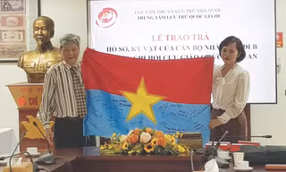 Ông Đỗ Trọng Văn đại diện cho các đồng nghiệp tặng lá cờ giải phóng có chữ ký của các cựu giáo viên đi B tại Trung tâm Lưu trữ Quốc gia III. Ảnh: KIẾN NGHĨA