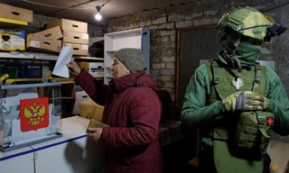 Một người dân đi bỏ phiếu vào thùng ngay cạnh lính gác ở thành phố Avdiivka, vùng Donetsk, ngày 16/3. (Ảnh: Reuters)