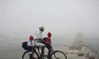 Một người đàn ông chở 2 con đi học bằng xe đạp giữa trời đầy sương mù ở Bhubaneswar, Ấn Độ
