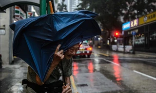 Một cụ bà che ô đứng đợi taxi tại Hồng Kông sáng 16/9. Ảnh: Getty