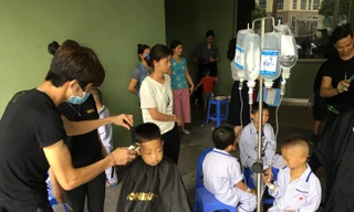 Nhiều bệnh nhi còn lủng lẳng bình dịch truyền xếp hàng ngồi chờ được cắt tóc. Ảnh: Đức Long