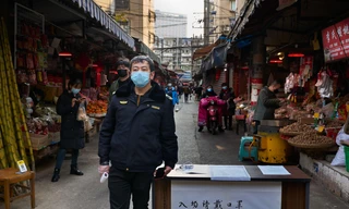 Nhân viên an ninh trực đo thân nhiệt tại cổng một chợ hải sản ở Vũ Hán ảnh: thesun.co.uk 